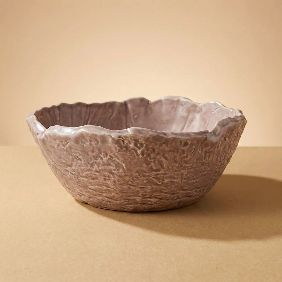 Ciotola artigianale in ceramica marrone con bordo irregolare e texture materica su sfondo neutro