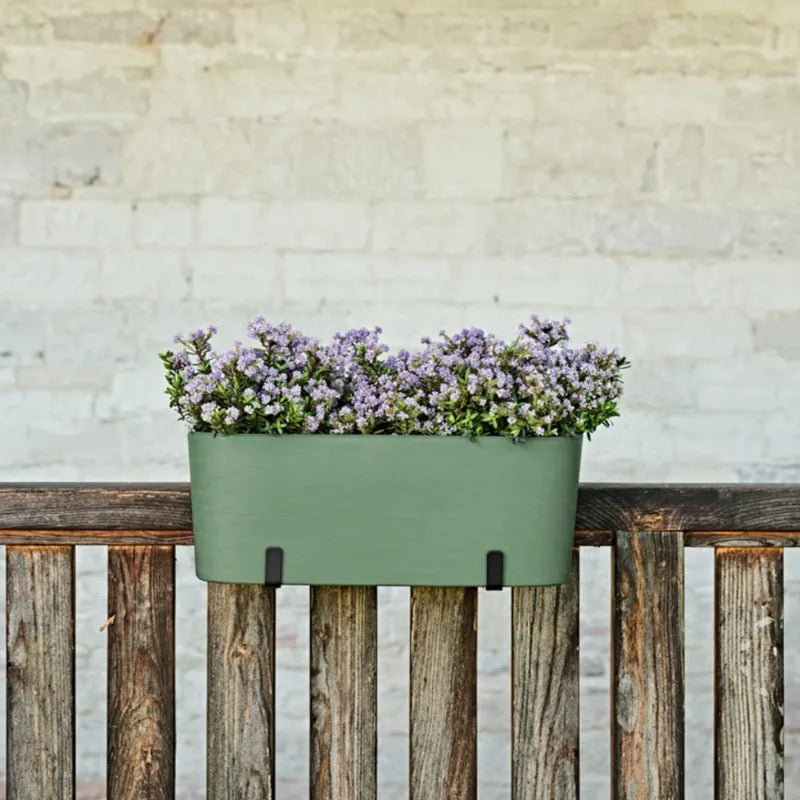 Fioriera Paros verde fissata a una staccionata in legno con fiori viola ornamentali per decorazioni da giardino e terrazzo.