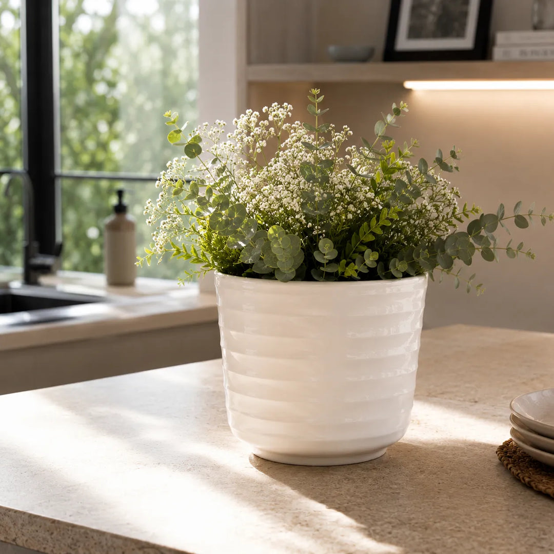 Vaso Cindy in ceramica bianca con composizione verde e fiori delicati, utilizzato come elemento decorativo su piano cucina luminoso.