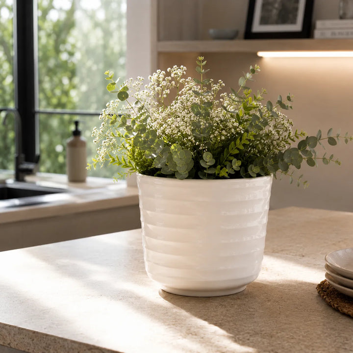 Vaso Cindy in ceramica bianca con composizione verde e fiori delicati, utilizzato come elemento decorativo su piano cucina luminoso.