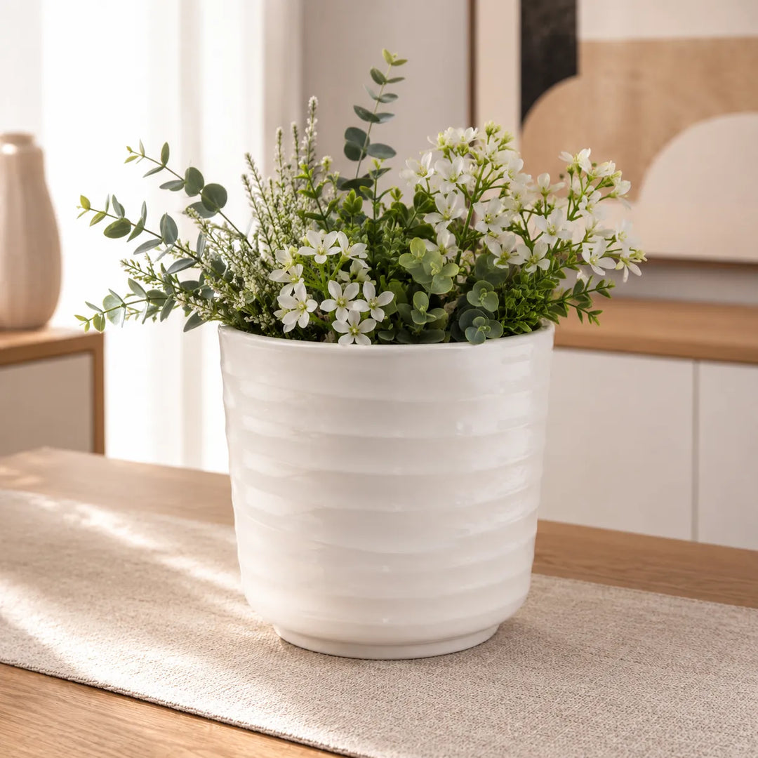 Vaso Cindy bianco con elegante composizione di fiori bianchi e foglie di eucalipto, perfetto per decorare tavoli e mobili in ambienti moderni.
