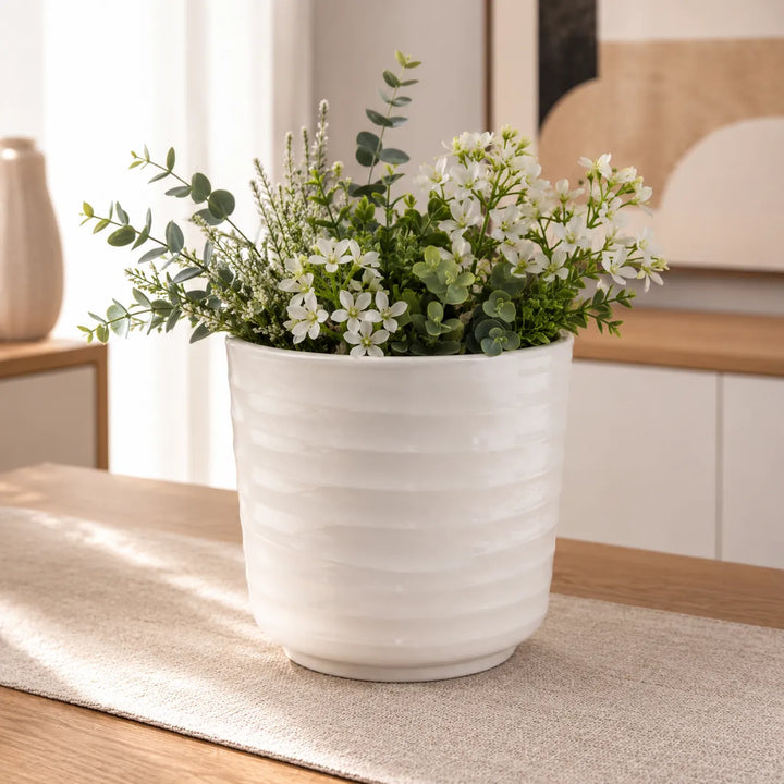 Vaso Cindy bianco con elegante composizione di fiori bianchi e foglie di eucalipto, perfetto per decorare tavoli e mobili in ambienti moderni.