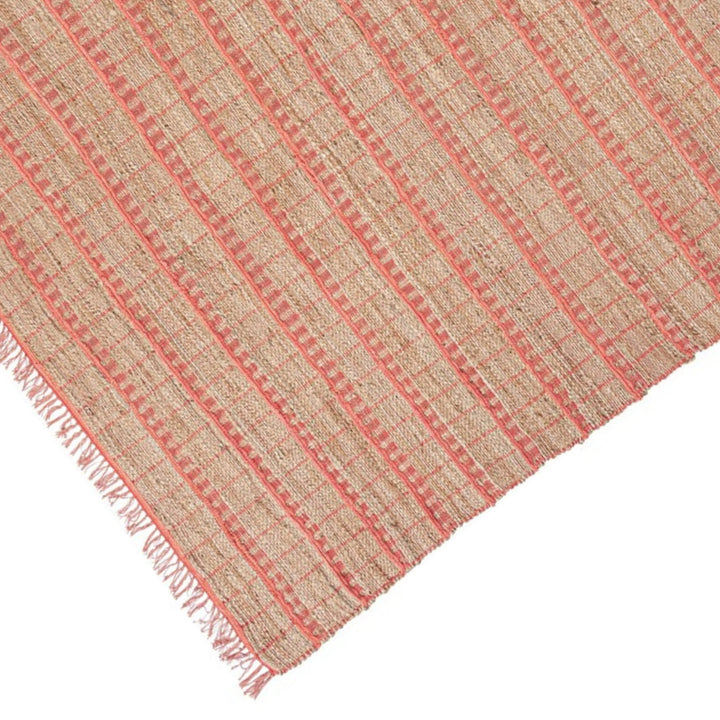 Dettaglio ravvicinato del tappeto in juta con texture intrecciata e linee rosa, evidenziate le frange e la lavorazione naturale.